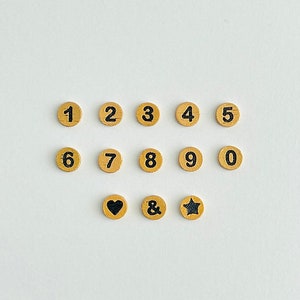 May include: A set of wooden craft supplies with numbers 1 through 9 and 0, an ampersand, a heart, and a star. The numbers, ampersand, heart, and star are black on a light brown background.
