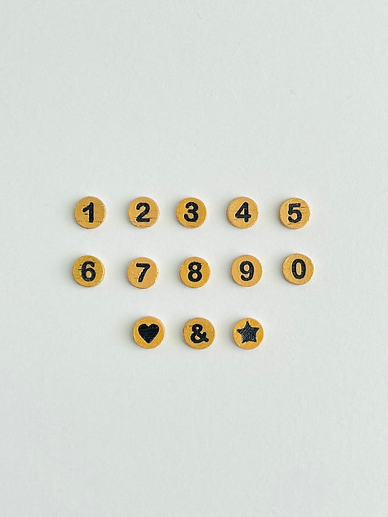 May include: A set of wooden craft supplies with numbers 1 through 9 and 0, an ampersand, a heart, and a star. The numbers, ampersand, heart, and star are black on a light brown background.