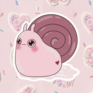 May include: A pink cartoon snail sticker with a dark pink shell and a small heart on its side. The snail has large, expressive eyes and rosy cheeks. The background features heart-shaped cookies with sprinkles, creating a whimsical and cute design.