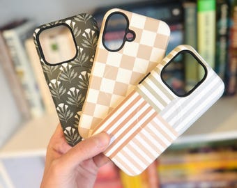May include: Three smartphone cases featuring distinct patterns: one dark green with white floral motifs, one with a beige and cream checkerboard design, and one with a multi-colored striped pattern in shades of peach, sage green, and white.