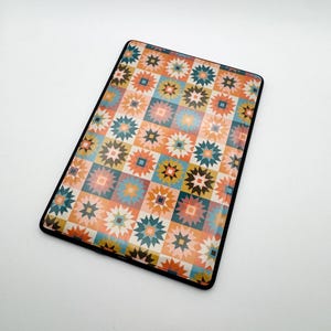 May include: Rectangular tablet case with a colorful geometric pattern in orange, teal, and brown. The design features star and square shapes arranged in a grid. The case has a black border and is set against a white background.
