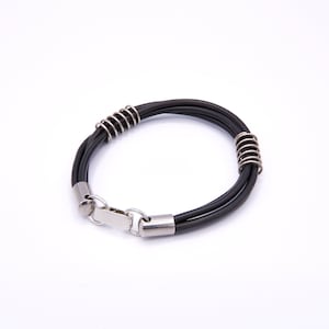 Może przedstawiać: Bransoletka ze skóry w kolorze czarnym z srebrnym zapięciem i srebrnymi detalami w kształcie spirali.