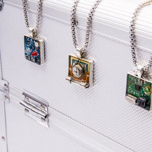 May include: Three silver necklaces with square pendants featuring different circuit board designs. The pendants are on a white background.