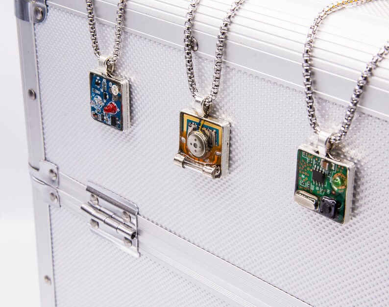 May include: Three silver necklaces with square pendants featuring different circuit board designs. The pendants are on a white background.