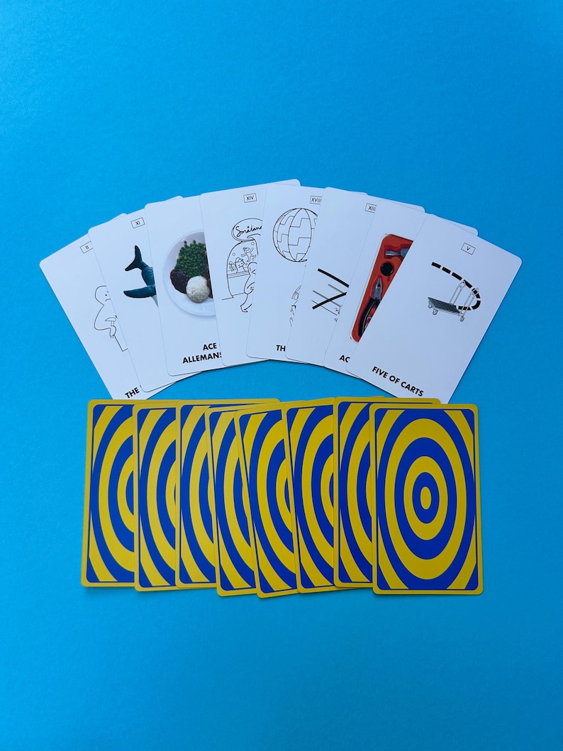 May include: A deck of playing cards with a blue and yellow concentric circle design on the back. The face-up cards feature black and white illustrations with text, including "ACE ALLEMAN!" and "FIVE OF CARTS", against a blue background.