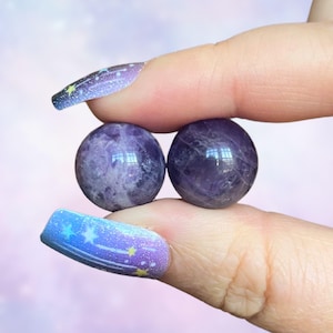 May include: Two amethyst spheres, one in each hand, against a purple and blue gradient background.