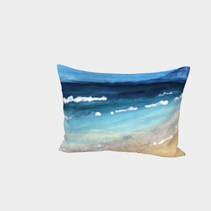 May include: A rectangular pillow with a painted image of a beach scene. The pillow features a blue and turquoise ocean with white foam waves and a sandy beach.