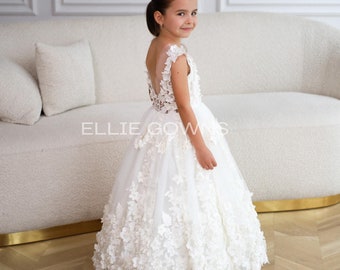 May include: A white floor-length gown featuring a sleeveless bodice with a deep V-back and intricate floral lace appliqués covering the skirt and shoulders. The text ELLIE GOWNS is visible in the centre of the image over the white dress.