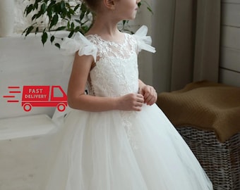 May include: A white tulle dress with lace detailing and a scalloped neckline. The dress has short sleeves with a ruffle detail and a full skirt.