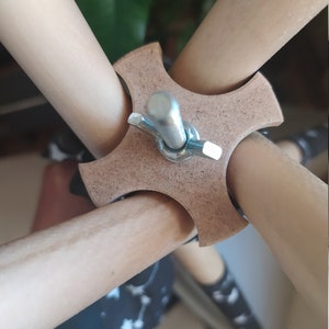 May include: Close-up of a wooden tripod stand with a metal screw connecting the legs. The stand is made of natural wood and has a simple design.