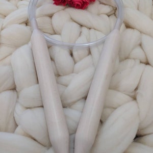 May include: A pair of white knitting needles with a clear plastic cable. The needles are lying on a white fluffy blanket.