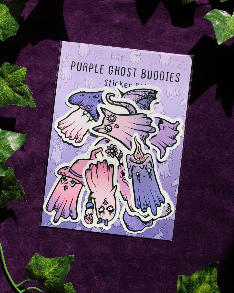 K&ouml;nnte beinhalten: Eine Packung Aufkleber mit verschiedenen lila Geister-Designs. Die Aufkleber zeigen Geister mit H&uuml;ten, Fl&uuml;geln und anderem Zubeh&ouml;r. Der Text "PURPLE GHOST BUDDIES" ist auf der Verpackung aufgedruckt. Die Aufkleber befinden sich auf einem lila Hintergrund.