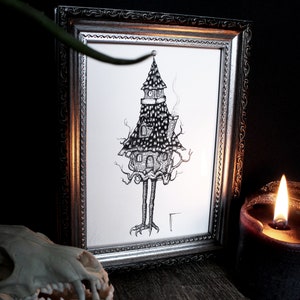 May include: A black and white ink drawing of a house with legs and a chimney, framed in a silver frame.