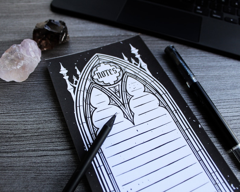 May include: Black and white notepad with a gothic arch design and the word "Notes" in a circle. The notepad has lined pages for writing.