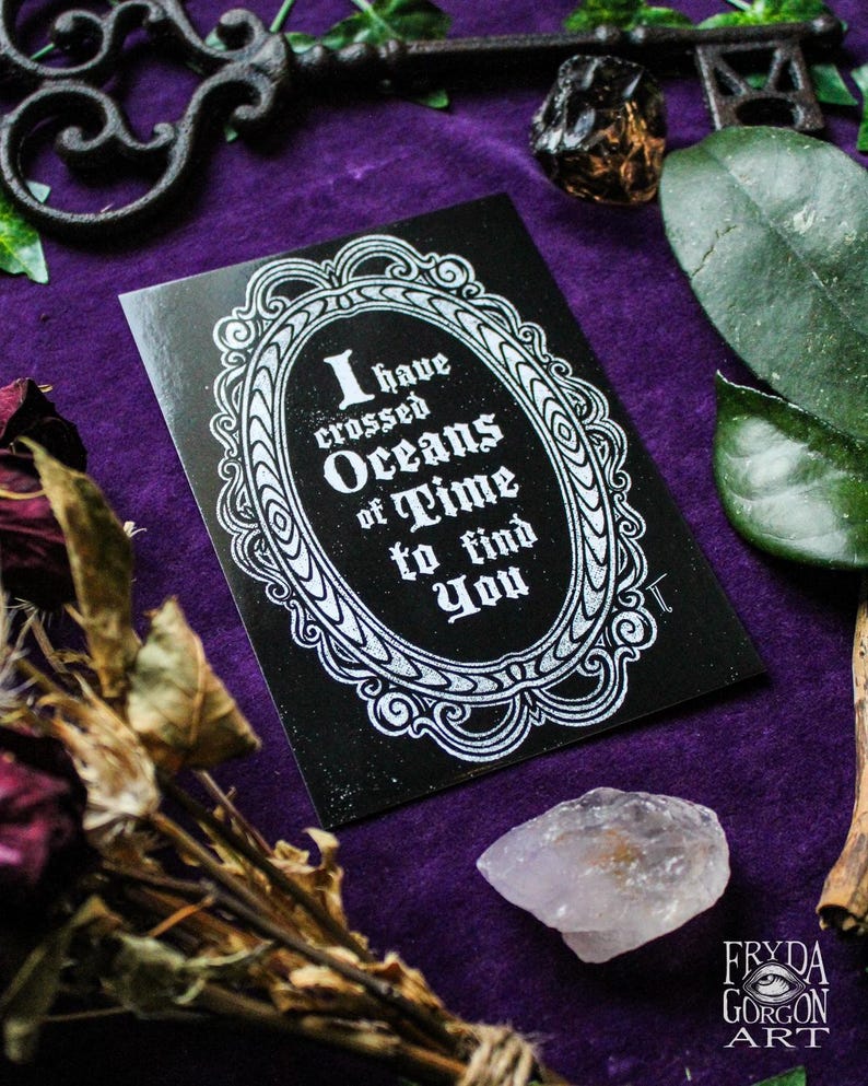 Puede incluir: Una tarjeta negra con un marco blanco adornado y el texto "He cruzado oc&eacute;anos de tiempo para encontrarte". La tarjeta est&aacute; sobre una superficie de terciopelo morado con una llave, un cristal y flores secas.