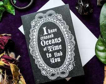 May include: A black greeting card with a white ornate oval frame surrounding the text I have crossed Oceans of Time to find You. The card is placed on a white envelope. The design features a gothic-style font and intricate border details.