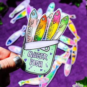 Könnte beinhalten: Ein holografischer Aufkleber, der eine hellgrüne Konservendose mit dem violetten Schriftzug QUEER FISH zeigt, verziert mit kleinen violetten Herzen und Fischsymbolen. In der Dose befinden sich vier bunte Fische mit glitzernden Schuppen.