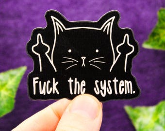 Może przedstawiać: Czarna naklejka z białym rysunkiem liniowym kota z dwoma podniesionymi środkowymi palcami. Tekst "Fuck the system." jest nadrukowany na biało pod kotem. Naklejka ma wykrojony kształt, który podąża za konturem kota i jego ramion.