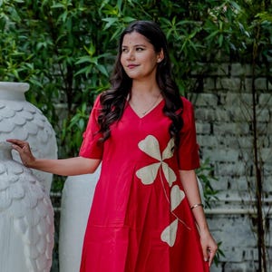 Puede incluir: Conjunto de vestido y pantalón rojo con cuello en V y mangas cortas. El vestido presenta un diseño floral en un color más claro. El atuendo se usa con sandalias negras. El estilo general es casual y elegante.