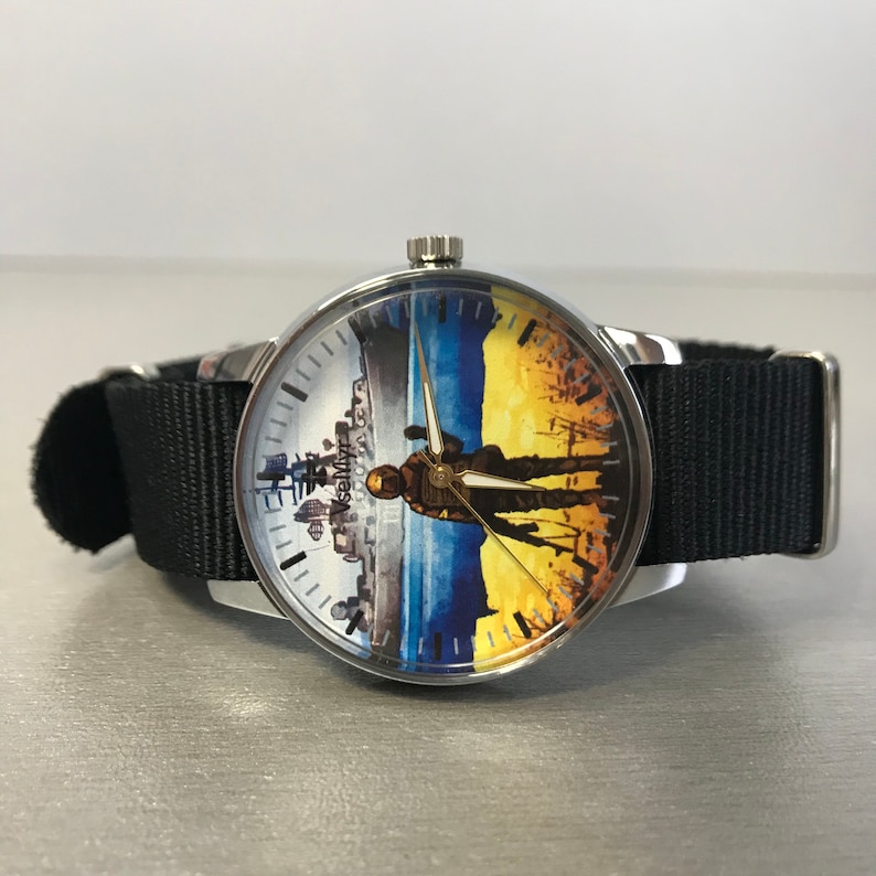 May include: A round wristwatch with a silver case and a black nylon band. The watch face features a split design with a cityscape on the left and a soldier silhouette against a yellow and blue background. The watch hands are gold.
