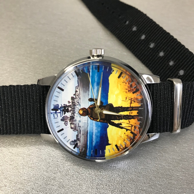 May include: A round wristwatch with a black nylon band. The watch face features a split design: a cityscape on the left and a soldier silhouette against a yellow and blue background on the right. The watch has silver-toned metal casing.