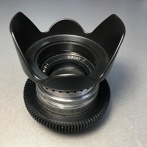 May include: A black lens hood is attached to a silver and black camera lens. The lens has the text "MIR-1" and "2.8/37" printed on it. The lens is made in the USA.