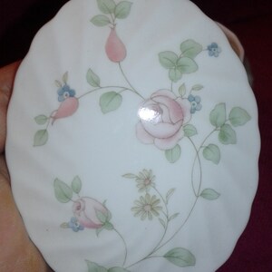 May include: A white ceramic trinket dish with a floral design featuring pink roses, green leaves, and blue flowers.