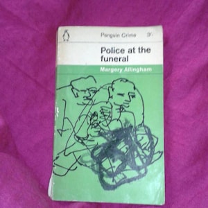 Puede incluir: Un libro de bolsillo verde con una ilustración en blanco y negro de dos personas en la portada. El título es "Police at the funeral" de Margery Allingham. El libro forma parte de la serie Penguin Crime.