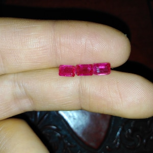 以下が含まれることがあります： ピンクの四角い宝石が指の上に並んでいます。おそらくルビーです。