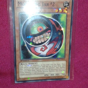 May include: A Magic: The Gathering card featuring a red and black monster with a large eye and a toothy grin. The card is titled "Mojar #2" and has an attack power of 800 and a defence power of 700. The card is from the Earth element.