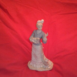 Hand painted porcelain ceramic figurine of a young woman in early 19th century period dress holding a cat with another cat at her feet