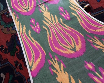 May include: A close-up of a green fabric with a repeating pattern of pink and yellow stylized flowers. The fabric is folded in half and the edges are visible.