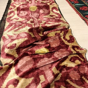 May include: A long, burgundy and gold patterned fabric with a velvet texture. The fabric is folded and draped on a light-colored surface.