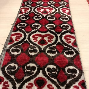 May include: A long piece of fabric with a repeating pattern of red, white, and black. The fabric has a woven texture and a slightly shiny finish.