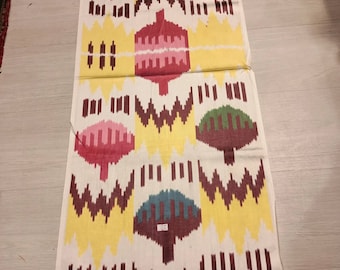 May include: A white fabric with a repeating pattern of colorful, abstract shapes. The shapes are in shades of red, pink, yellow, green, brown, and blue. The fabric has a woven texture.