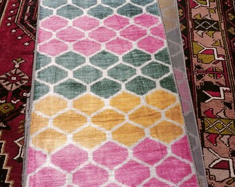 May include: A colorful rug with a geometric pattern of hexagons in shades of pink, yellow, and green. The rug has a white background and is made of a soft, luxurious material.