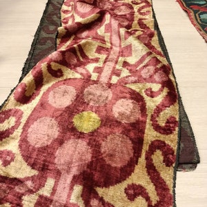 May include: A close-up of a red and gold fabric with a floral pattern. The fabric is folded and has a textured surface.