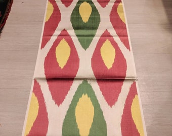 May include: A white fabric with a repeating pattern of red, yellow, and green diamond shapes. The fabric has a subtle sheen and a soft texture.