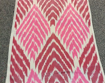 May include: A rectangular textile with a repeating chevron pattern in shades of pink and red on a cream background. The fabric is folded and lies flat, showcasing the intricate design. Ideal for home decor.