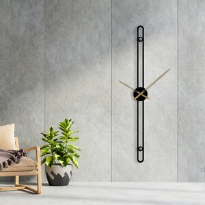 Könnte beinhalten: Eine moderne Wanduhr in Schwarz und Gold mit einem langen, dünnen, vertikalen Design. Die Zeiger der Uhr sind golden und das Zifferblatt ist schwarz. Die Uhr ist an einer grauen Betonwand montiert.