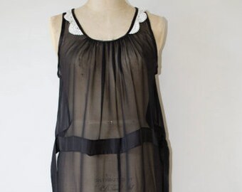 May include: A black, sheer dress with a layered design. The dress features a scoop neckline with white lace trim and a flowing, asymmetrical hemline. The dress is displayed on a mannequin.