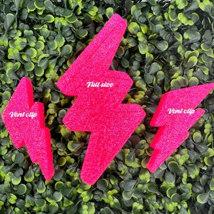 May include: Three pink glitter lightning bolt car air freshener charms. The largest charm says "Full size" and the two smaller charms say "Vent clip".