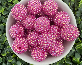Op de afbeelding: Een kom gevuld met roze, iriserende ronde kralen. De kralen zijn bedekt met kleine strass steentjes.