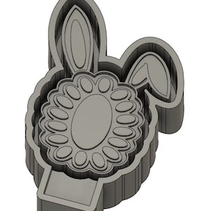 Op de afbeelding: Een grijze 3D-geprinte koekjesvorm in de vorm van een konijn met een bloem om zijn hoofd. De vorm heeft een grote ovale vorm in het midden voor een koekje.
