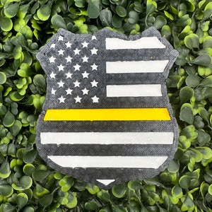 May include: A black and white American flag with a yellow stripe across the middle, in the shape of a police badge.