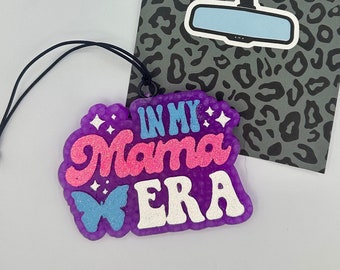 Könnte beinhalten: Ein lila glitzernder Auto-Lufterfrischer aus Harz, der an einer schwarzen Schnur hängt. Der Text IN MY Mama ERA ist in blauem, rosa und weißem Glitzer gestaltet. Ein kleiner blauer Schmetterling und weiße Sterne sind eingeprägt. Befestigt auf einer grauen Leoparden-Karte.