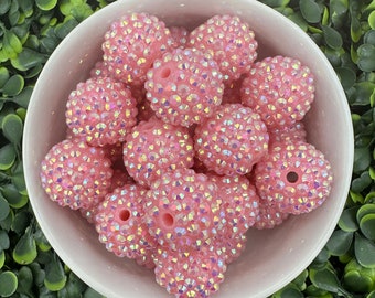 Op de afbeelding: Een kom met roze iriserende kralen met een glinsterende afwerking. De kralen zijn rond en hebben een gat in het midden.