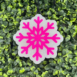 May include: A white snowflake ornament with a pink glitter finish. The snowflake is a simple design with six points.