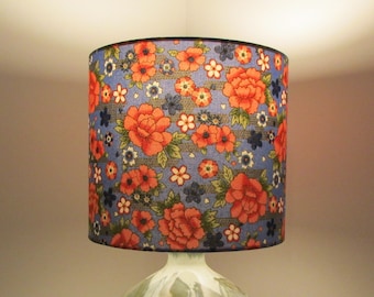 May include: A blue lampshade with a floral pattern featuring red and white flowers. The lampshade is cylindrical and has a black trim.