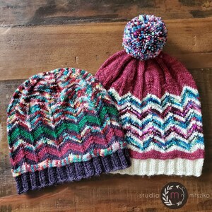 May include: Two knitted hats with colorful chevron patterns. One hat has a burgundy crown and a white brim with a multi-colored pom-pom on top. The other hat has a purple brim and a multi-colored crown.